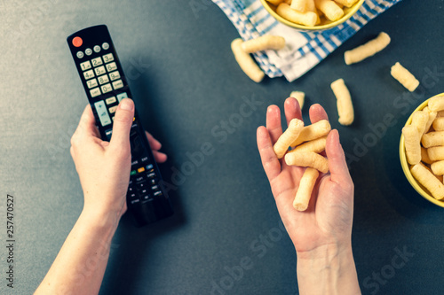 Person with TV remote watching a tv and eating chips