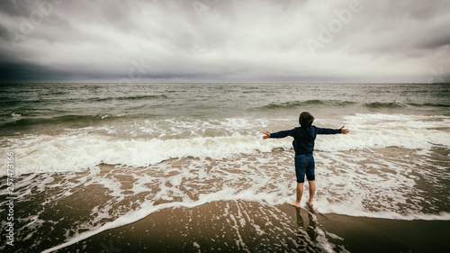 Kind steht am Strand und breitet die Arme aus