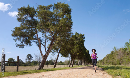 A wide shot of a young woman running down a dirt road lined with evergreen trees in Demopolis, Alabama. photo