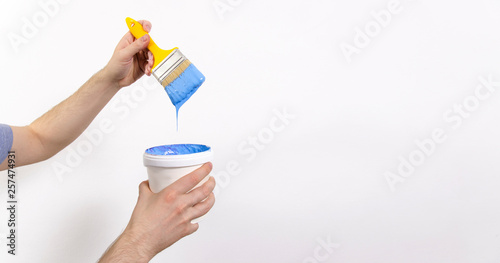 Man holding yellow brush dipped in in blue paint, copy space, painter job 