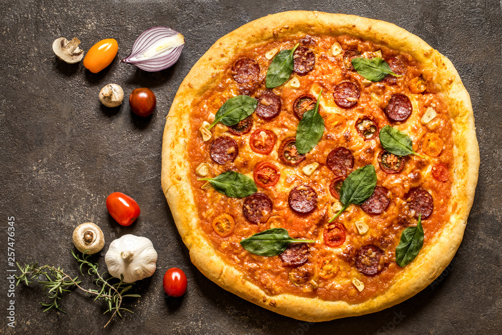 pizza with salami sausage, spinach and cherry tomatoes and tomato sauce on a dark background