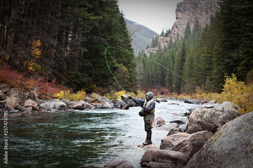 A athletic man fly fishing stands on the banks of the Gallatin River surrounded with the fall colors in Bozeman, Montana. photo