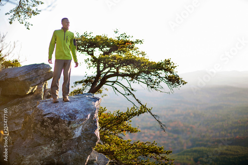 A youn man smiles while looking off a rock overhang at Cheaha Mountain. photo