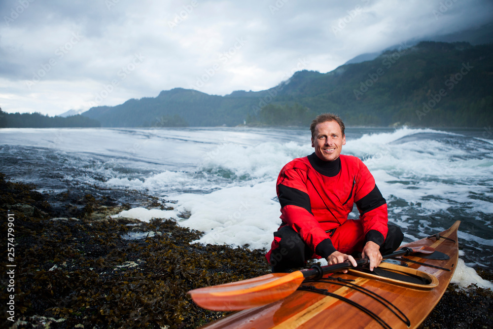 Man crouching next to Cedar strip kayak Man crouching next to Cedar strip kayak