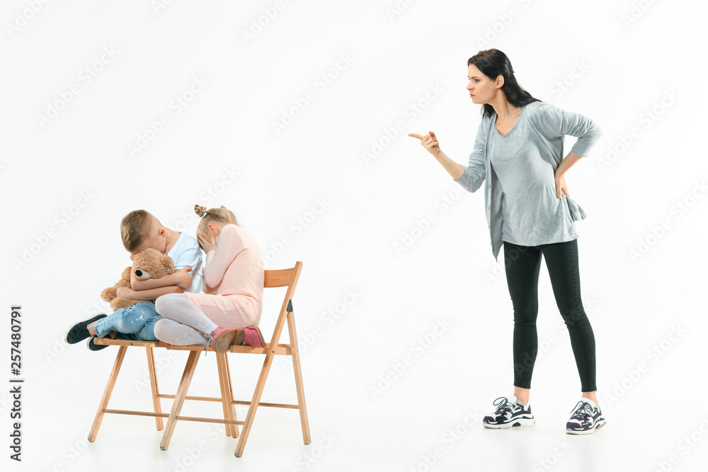 Obraz premium Angry mother scolding her son and daughter at home. Studio shot of emotional family. Human emotions, childhood, problems, conflict, domestic life, relationship concept