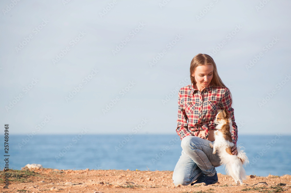 happy smiling young caucasian female in plaid shirt and jeans with her small pet chihuahua dog on sea coast happy smiling young caucasian female in plaid shirt and jeans with her small pet chihuahua dog on sea coast