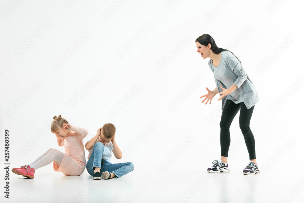 Angry mother scolding her son and daughter at home. Studio shot of emotional family. Human emotions, childhood, problems, conflict, domestic life, relationship concept