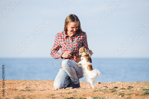 happy smiling young caucasian woman in plaid shirt and jeans playing with her small pet chihuahua dog on sea shore © ruslanshug