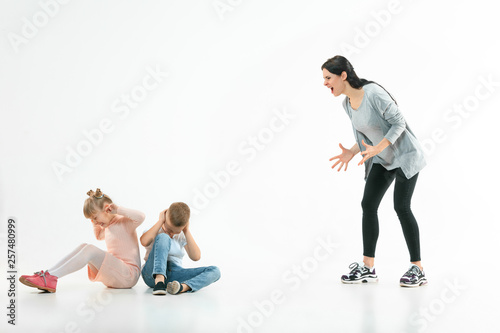 Angry mother scolding her son and daughter at home. Studio shot of emotional family. Human emotions, childhood, problems, conflict, domestic life, relationship concept
