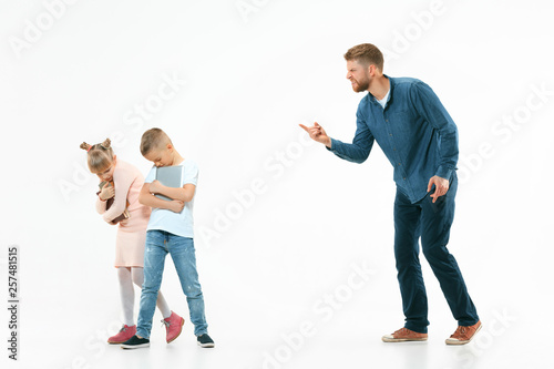 Angry father scolding his son and daughter at home. Studio shot of emotional family. Human emotions, childhood, problems, conflict, domestic life, relationship concept