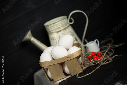 set of white raw eggs in a basket and a jug on a dark background