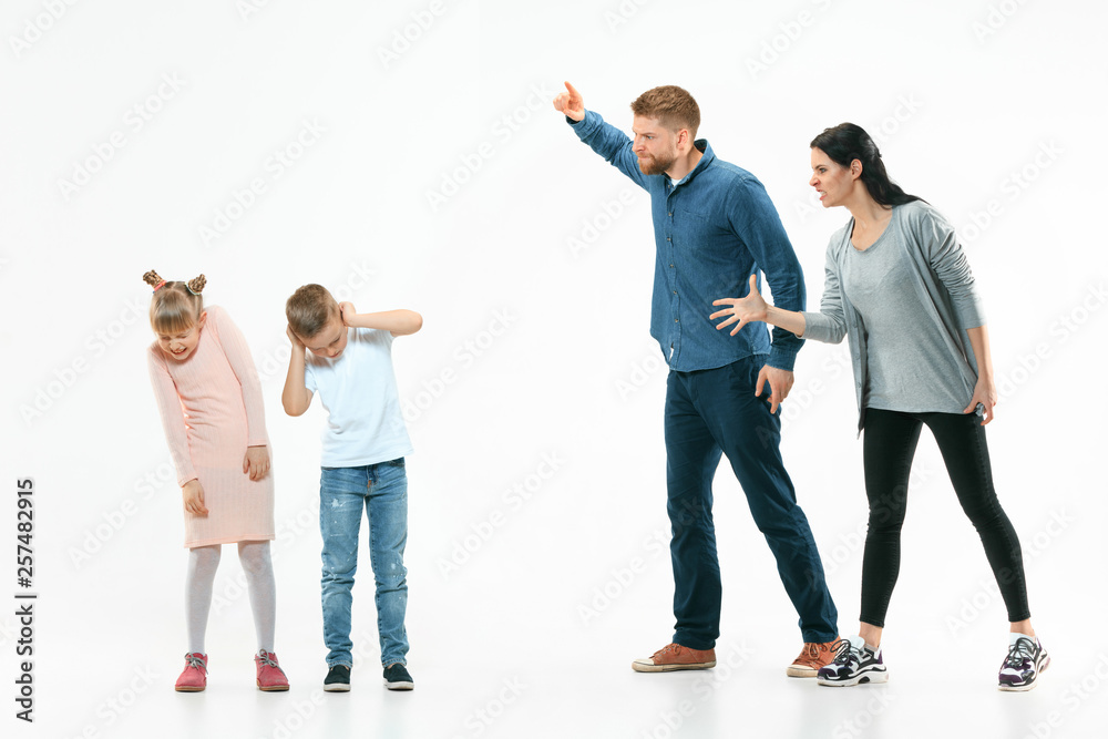 Angry parents scolding their children - son and daughter at home. Studio shot of emotional family. Human emotions, childhood, problems, conflict, domestic life, relationship concept