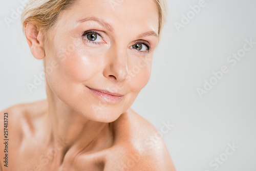attractive and blonde mature woman looking at camera on grey background