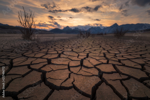 Earth cracked by extreme drought below a dramatic sunset. photo