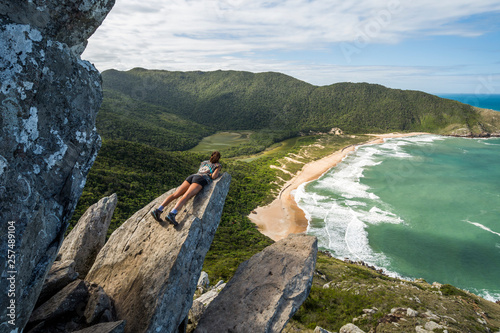 Young woman lying on edge of rock with view from Pico da Coroa Hill to Lagoinha do Leste Beach, Florianopolis, Santa Catarina Island, Brazil  photo