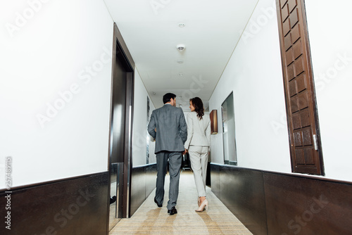 confident businessman businesswoman in formal wear holding hands and walking in hotel corridor
