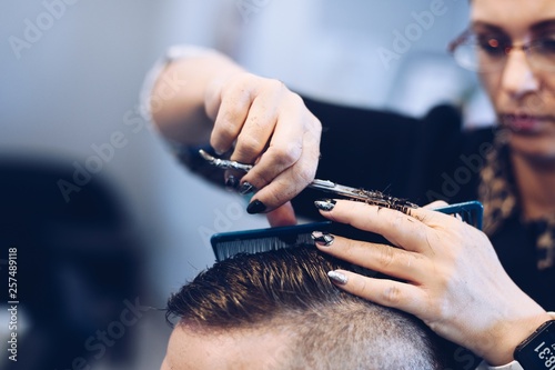 Woman hairdresser cutting man's hair with scissors.