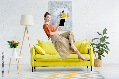 elegant happy young woman levitating in air and showing digital tablet with blank screen in living room photo