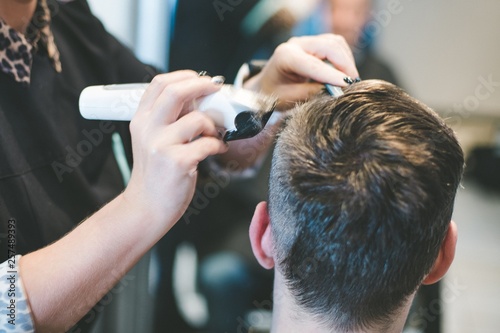 Hairdresser cutting man's hair with electric trimmer