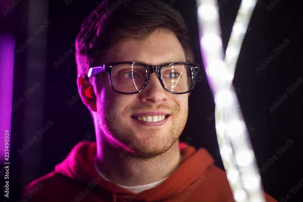 vision, eyewear and people concept - portrait of smiling young man in glasses over ultra violet neon lights in dark room vision, eyewear and people concept - portrait of smiling young man in glasses over ultra violet neon lights in dark room