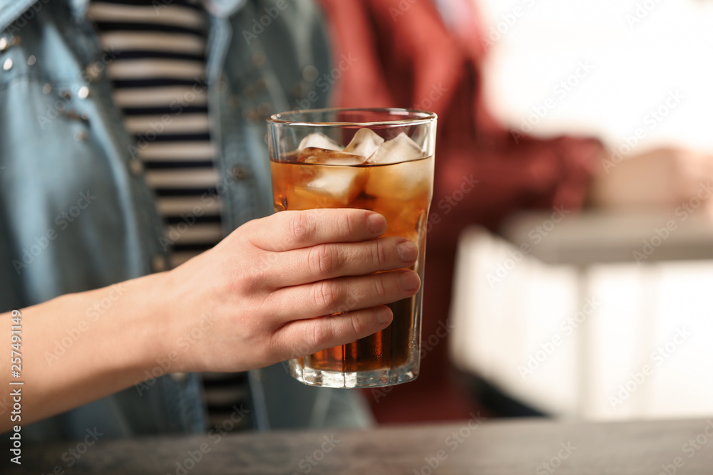 Woman holding glass of cola with ice at table, closeup. Space for text