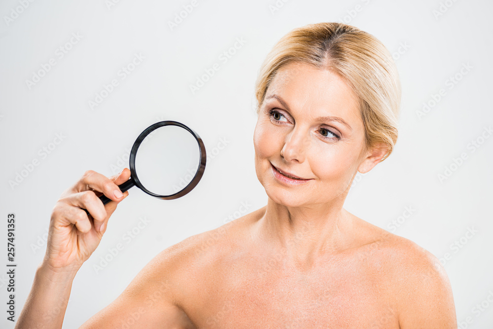 beautiful and blonde mature woman holding loupe and looking away on grey background beautiful and blonde mature woman holding loupe and looking away on grey background