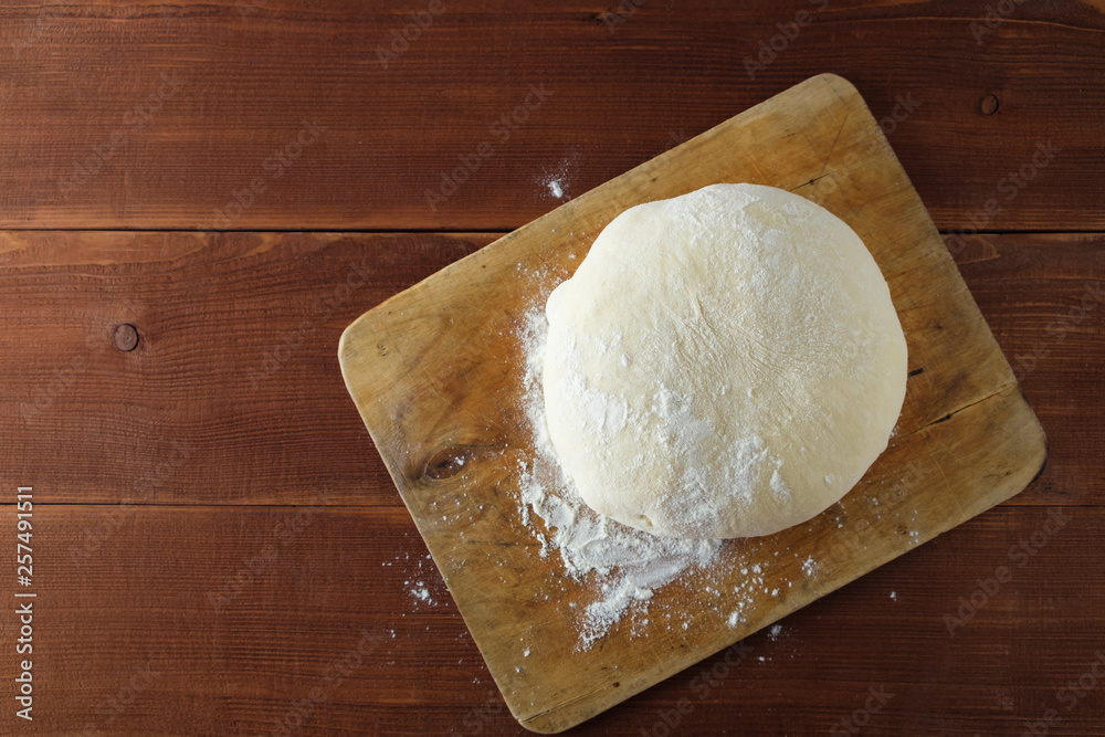 Classic wooden rolling pin with freshly prepared dough and dusting of flour on wooden background Classic wooden rolling pin with freshly prepared dough and dusting of flour on wooden background