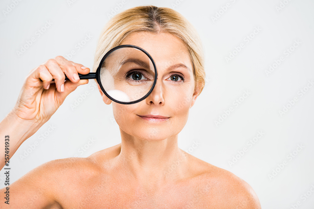 beautiful and blonde mature woman looking at camera and holding loupe on grey background beautiful and blonde mature woman looking at camera and holding loupe on grey background
