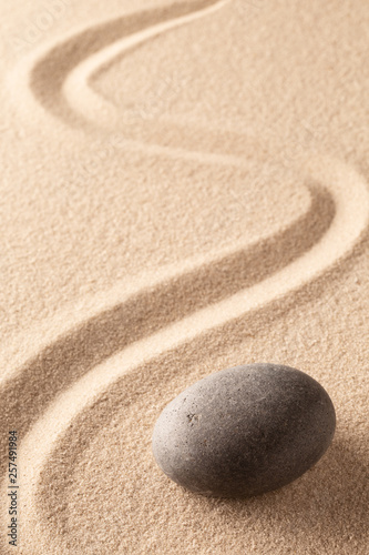 curved line in the sand of a zen stone garden. A round black rock on sandy background. Concept for spirituality, harmony and balance.