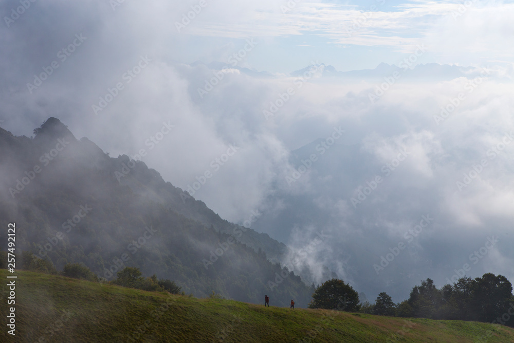 Two hikers on a mountain trail surrounded by mist and clouds. Hiking the Sentiero delle Orobie in the Italian Alps Two hikers on a mountain trail surrounded by mist and clouds. Hiking the Sentiero delle Orobie in the Italian Alps