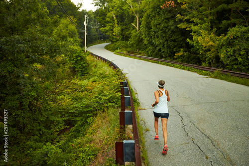 A woman runs up a hill along a country road. 