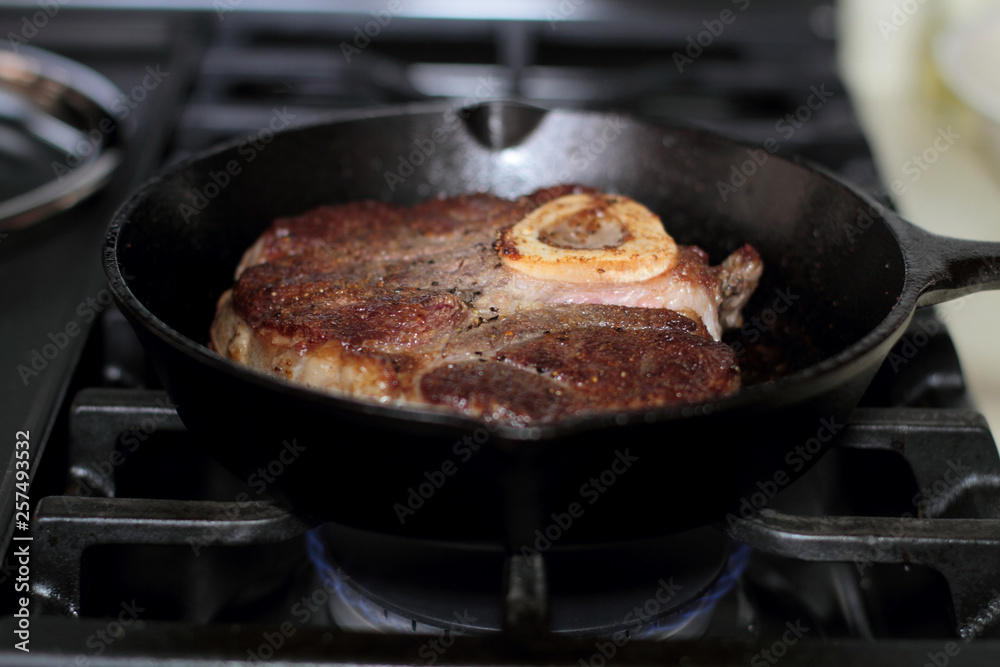 Shank steak frying in a cast iron pan.