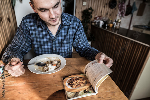 Man reading cookbook while eating meal at home photo