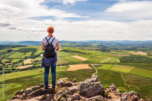 Redhead girl enjoying the view from the top of the Great Sugar Loaf Mountain in Wicklow, Ireland. Beautiful vibrant green Irish landscape on a lovely summer day.