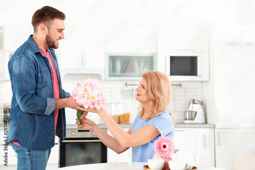 Fototapeta premium Young man congratulating his mature mom in kitchen, space for text. Happy Mother's Day