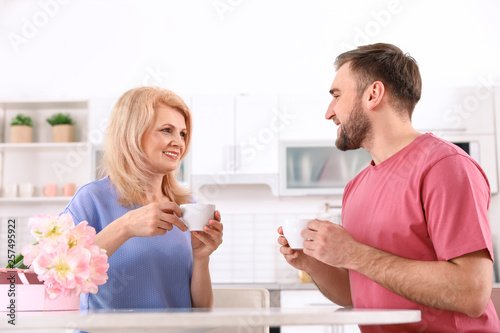 Young man and his mature mom having breakfast in kitchen. Happy Mother's Day