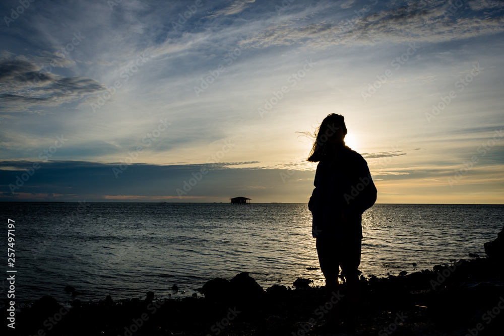 Silhouette of a girl standing alone on seashore with beautiful sky on the background at Harapan Island, Indonesia Silhouette of a girl standing alone on seashore with beautiful sky on the background at Harapan Island, Indonesia