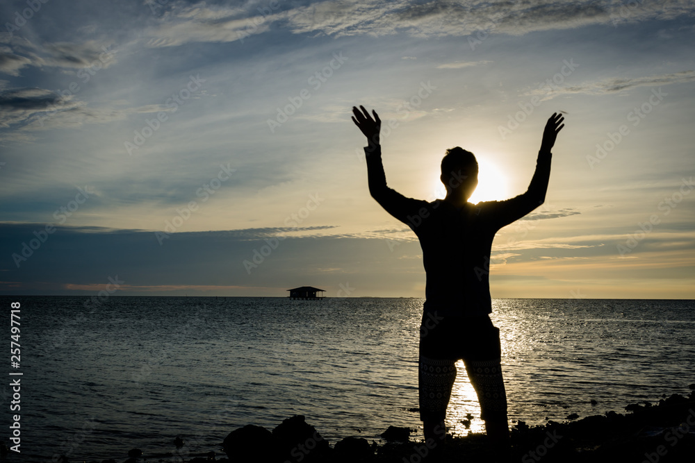 Silhouette of a man standing alone and posing on seashore with beautiful sky on the background at Harapan Island, Indonesia Silhouette of a man standing alone and posing on seashore with beautiful sky on the background at Harapan Island, Indonesia
