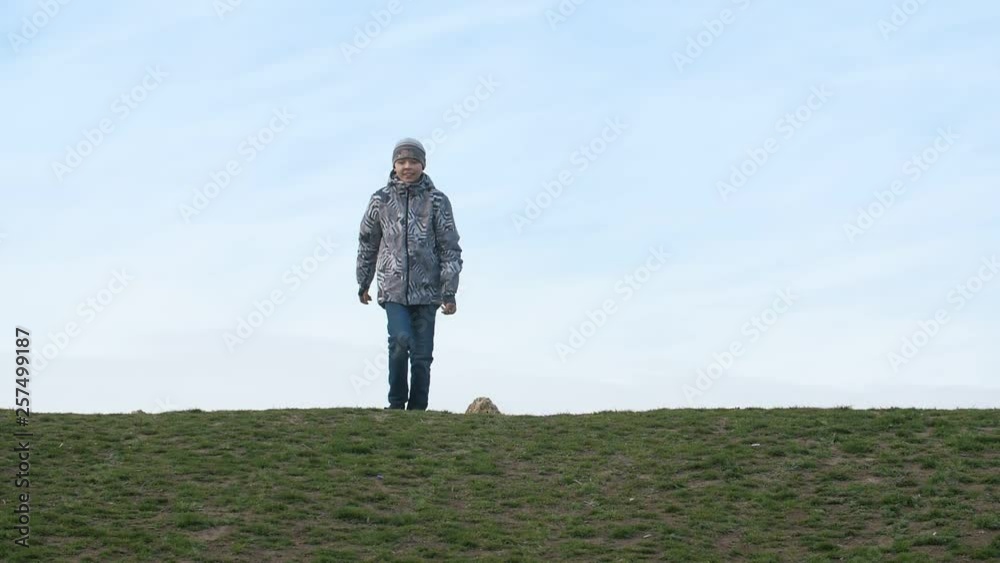 Cheery kid in a jacket running and jumping up in a field on a sunny day in slo-mo Cheery kid in a jacket running and jumping up in a field on a sunny day in slo-mo