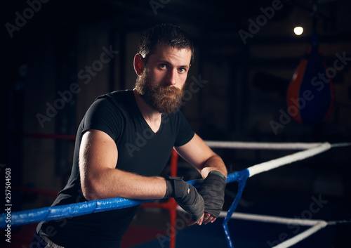 Portrait of handsome sportsman kick boxer standing in the ring at the health club after hard practicing kickboxing