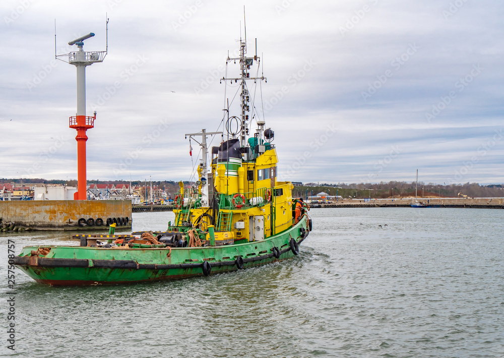 Tug boat, yellow-green color, entering the harbour.