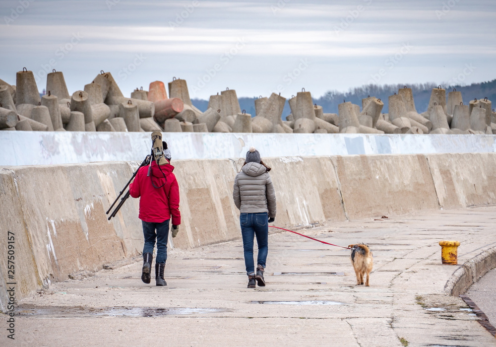 Young couple with dog, walking on the pier, man is carry telescope for birds watching