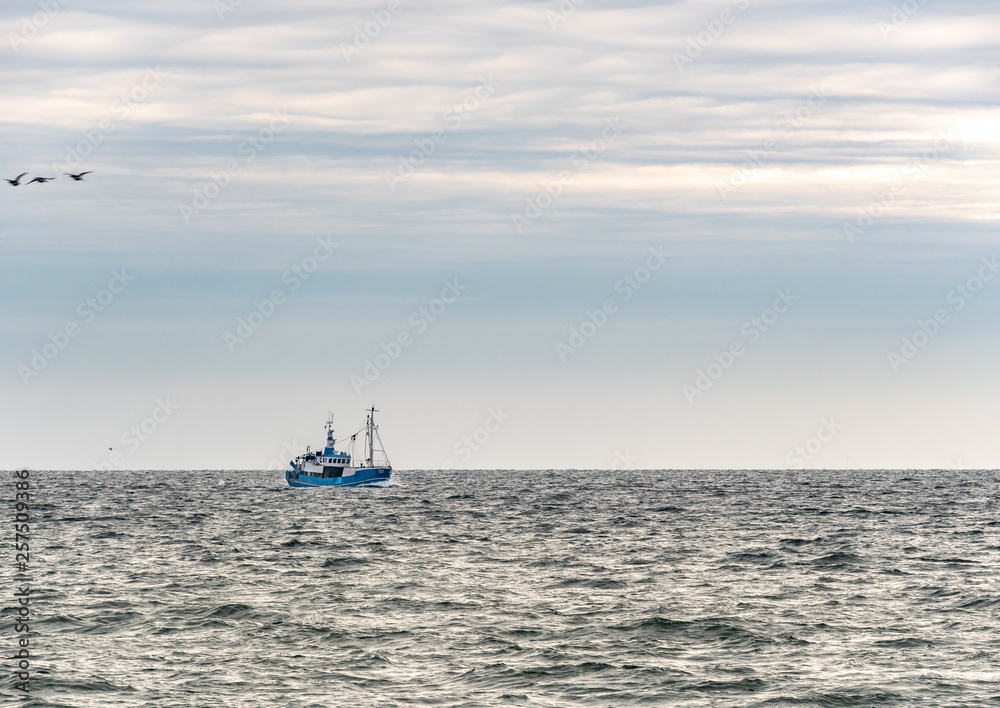 Small single fishing boat at the open sea with scenic sky.