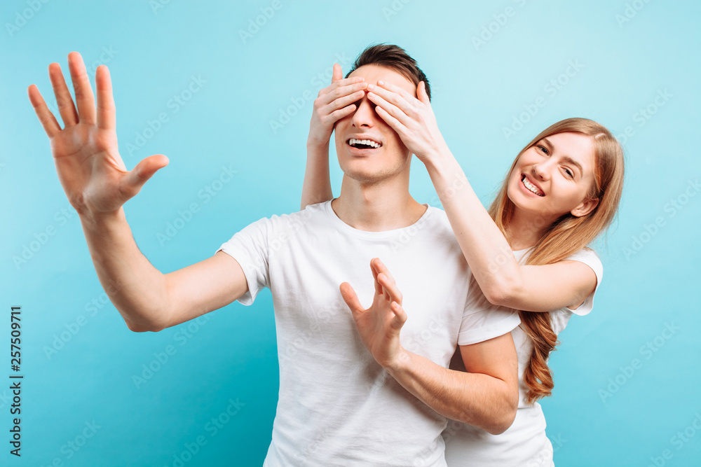 of a loving couple, a man and a woman, dressed a woman closes the eyes of a guy, wants to make a surprise, on a blue background