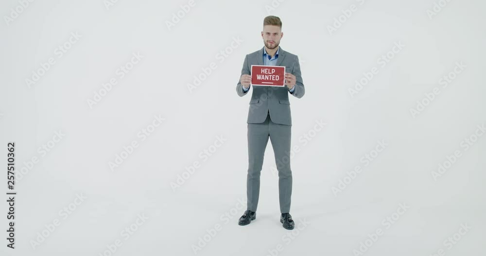 FIXED Handsome Caucasian HR manager wearing suit holding recruitment sign saying Help Wanted. Light grey background. 4K UHD FIXED Handsome Caucasian HR manager wearing suit holding recruitment sign saying Help Wanted. Light grey background. 4K UHD