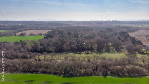 An aerial view of a scenic rural area with a forest in the middle of green fields under a majestic blue sky