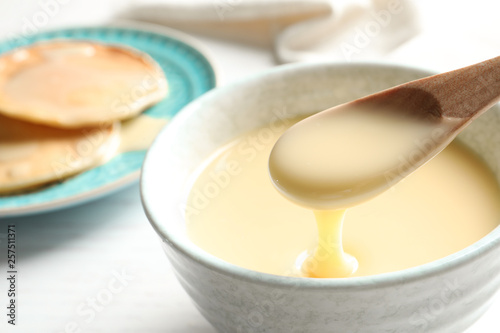 Spoon of pouring condensed milk over bowl on table  closeup with space for text. Dairy products