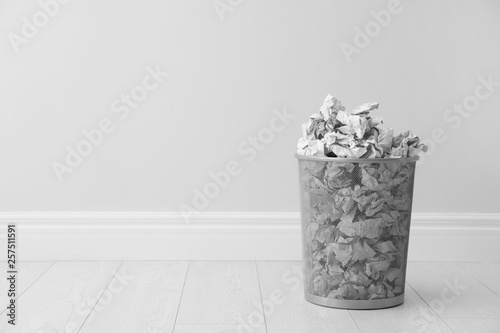 Metal bin and crumpled paper against light wall, space for text