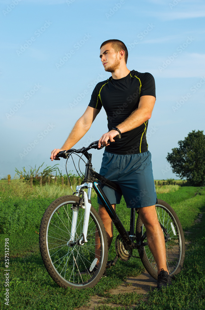 guy brunette in gym clothes. training in the field. sitting on the bike guy brunette in gym clothes. training in the field. sitting on the bike
