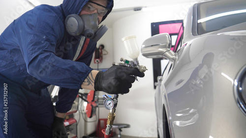 Принти на полотні In slow motion, a Man (Man) professional in working uniform with spray guns in his hands and a respirator in protective glasses puts paint (ceramics) on the car on different parts of the car